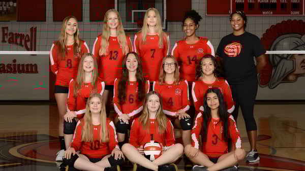 Un grupo de jóvenes jugadoras de voleibol en camisetas rojas en el Paradise Valley Unified School District posan en el gimnasio.
