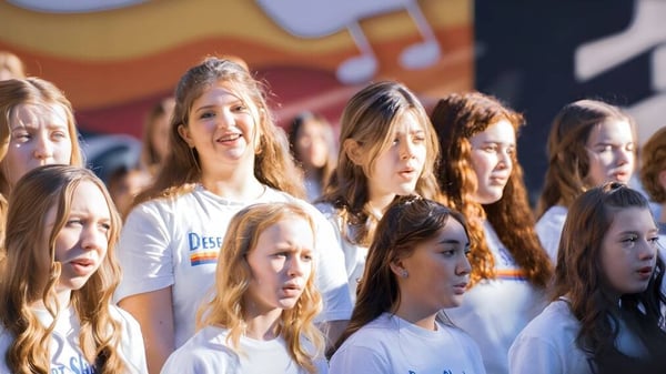 Un grupo de estudiantes del Paradise Valley Unified School District está junto en una sala con notas musicales e instrumentos de fondo.
