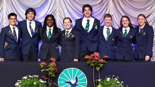 Estudiantes de Paraparaumu College están en uniformes escolares en un escenario con un arreglo floral y cortina al fondo.