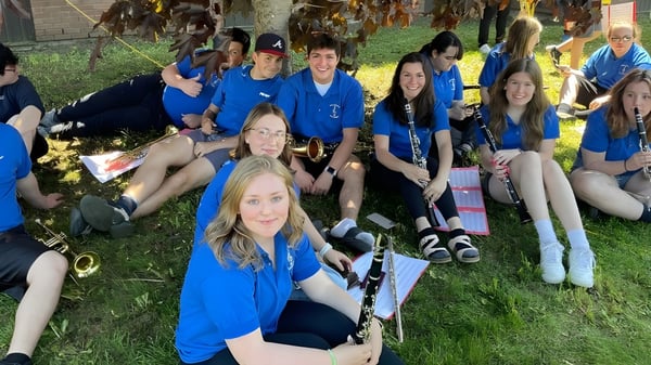Un grupo de estudiantes de la Pasadena Academy está afuera en un prado frente a unos árboles.