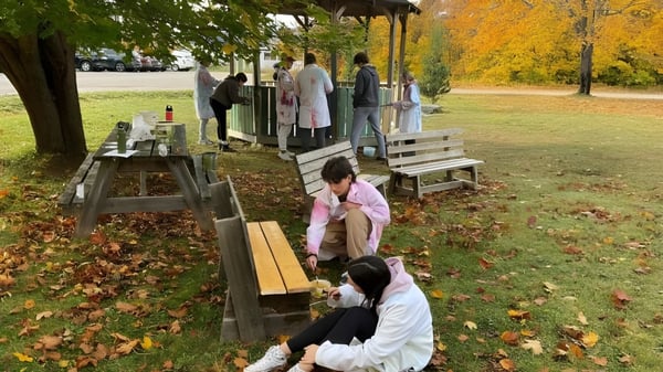 Un grupo de estudiantes de la Pasadena Academy está de pie sobre una plataforma de madera en el parque otoñal.