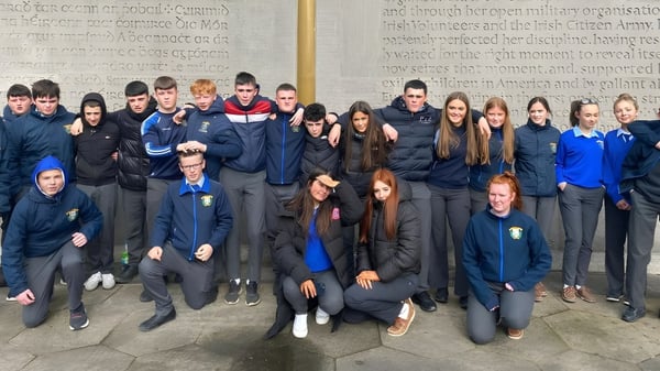 Un grupo de estudiantes está frente a una pared con un letrero en el campus de la Patrician Presentation Secondary School.