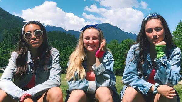 Tres alumnas de la Pemberton Secondary School están sentadas juntas al aire libre con montañas y bosque de fondo.