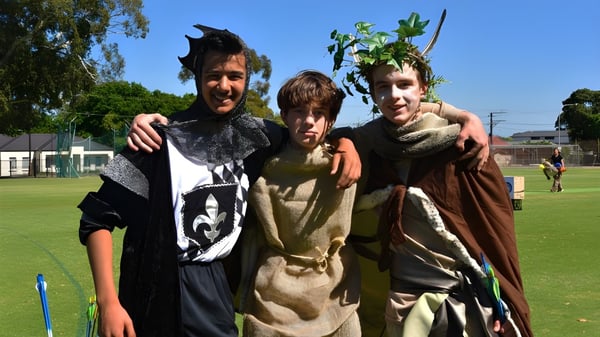 Tres personas disfrazadas están de pie en un campo bajo un cielo azul en el terreno de la Pembroke School.