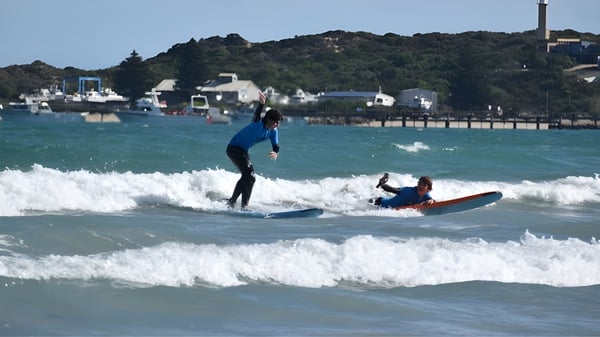 Un estudiante de la Pembroke School surfea en las olas frente a una pintoresca ciudad costera.