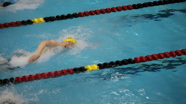 Un nadador con gorra de baño amarilla nada en la piscina de competición en el terreno de la Penticton Secondary School.