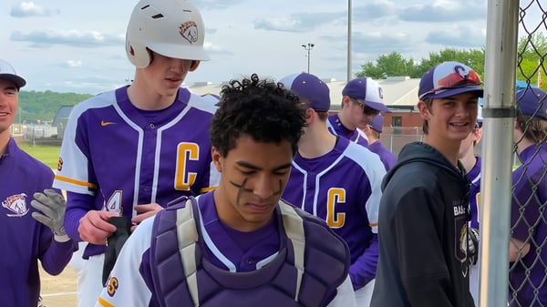Un grupo de jóvenes beisbolistas en uniformes morados está en el campo de béisbol de la Peoria Christian School.