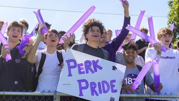 Un grupo de estudiantes de la Perkiomen School sostiene banderas moradas y carteles en una celebración del orgullo al aire libre.