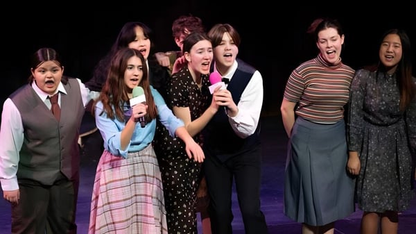 Estudiantes de la Phillips Academy están juntos en el escenario realizando una actuación de canto frente a un fondo oscuro.