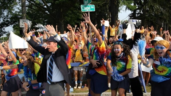 Un gran grupo de estudiantes de la Phillips Academy se reúne afuera con los brazos en alto.