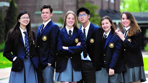 Un grupo de estudiantes con uniforme escolar está frente a un edificio en el campus del Pickering College.