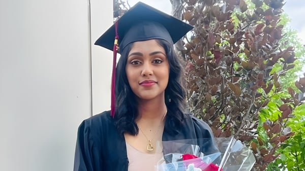 Una joven en traje de graduación está frente a un fondo verde en el campus de la Pine Ridge Secondary School.