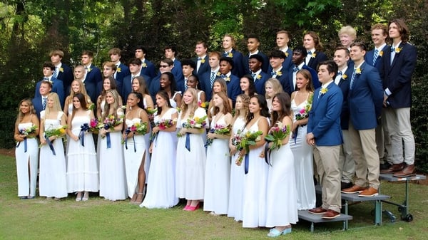Un grupo de estudiantes de la Pinewood Preparatory School está junto en ropa formal en un área verde al aire libre.