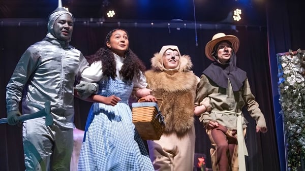 Cuatro estudiantes de la Pinewood Preparatory School están disfrazados en el escenario frente a un fondo iluminado.