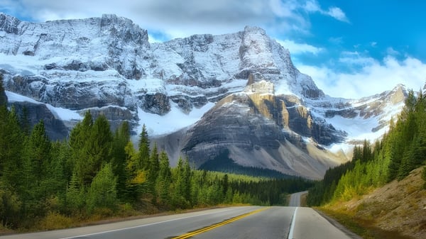 Una carretera sinuosa atraviesa un valle boscoso hacia montañas cubiertas de nieve en el campus de la Pitt Meadows Secondary School.