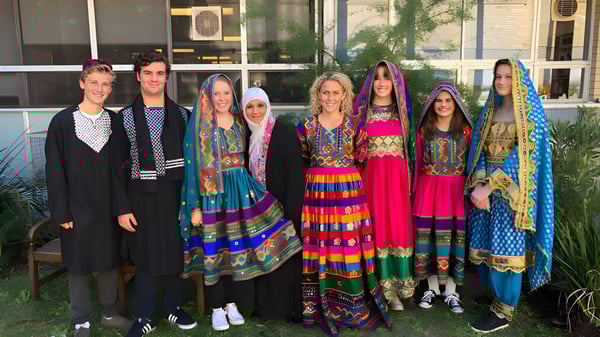 Un grupo de mujeres con vestidos tradicionales coloridos está frente a un edificio en el campus de la Pittwater High School.