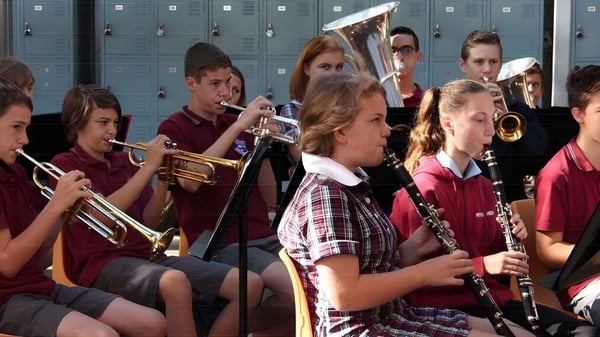 Estudiantes de la Pittwater High School están con instrumentos musicales en el pasillo escolar frente a los casilleros.