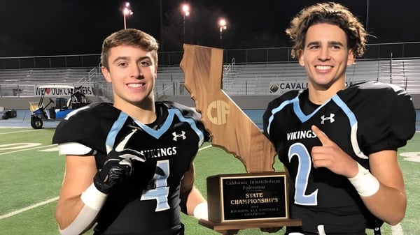 Dos estudiantes de la Pleasant Valley High School en uniforme deportivo sostienen un trofeo en el campo de deportes.
