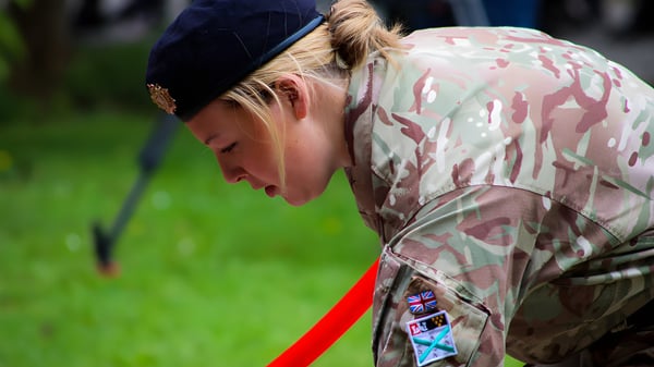 Una persona en uniforme de camuflaje militar está de pie en un prado en el terreno del Plymouth College con la cabeza agachada.