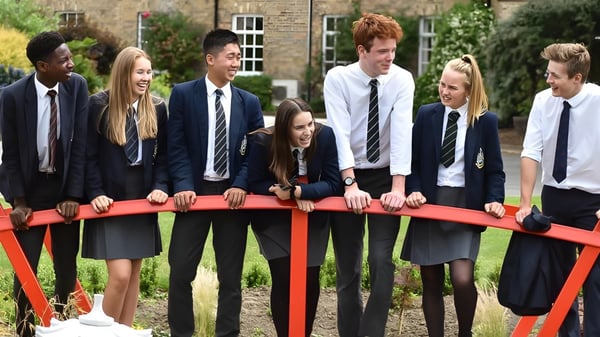 Un grupo de estudiantes de la Pocklington School está en un puente rojo frente a un edificio de ladrillo al aire libre.