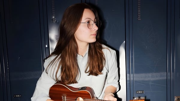 Una estudiante de la Polyvalente Roland-Pépin sostiene una guitarra acústica frente a una pared azul oscura.
