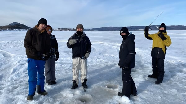 Un grupo de estudiantes de la Polyvalente Roland-Pépin está vestido para el invierno sobre un lago congelado con fondo montañoso.