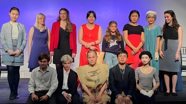 Un grupo de estudiantes se encuentra de pie y sentados en un escenario con fondo púrpura en la Pomfret School.