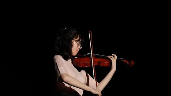 Una alumna de la Port Hacking High School toca un violín en una habitación débilmente iluminada.