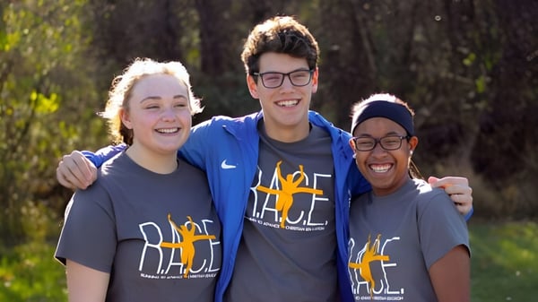 Tres estudiantes están sonriendo en el bosque en el terreno de la Portland Christian High School.