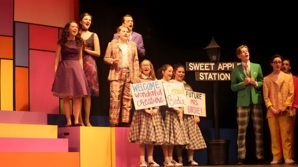 Un grupo de alumnos está en el escenario del Portlaoise College durante un evento con el letrero Sweet Apple Station de fondo.