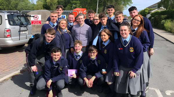 Un grupo de estudiantes en uniformes escolares está de pie y sentado en el área exterior de la Portmarnock Community School.