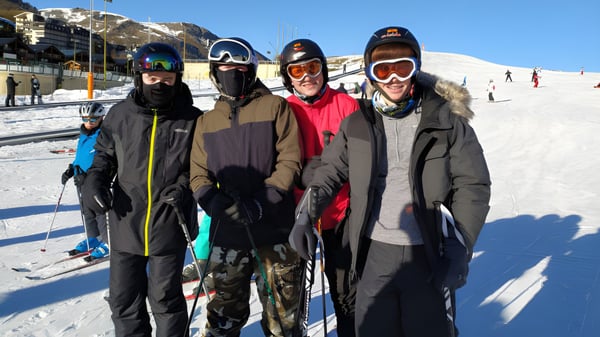 Un grupo de cuatro estudiantes de la Portmarnock Community School está de pie con ropa de invierno en una pendiente nevada frente a montañas.