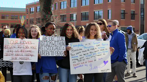 Un grupo de jóvenes sostiene carteles con mensajes sociales y políticos frente a un edificio de ladrillo en el campus de Poudre School District.