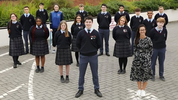 Un grupo de estudiantes del Presentation College Carlow está reunido en un área exterior pavimentada con zonas verdes.