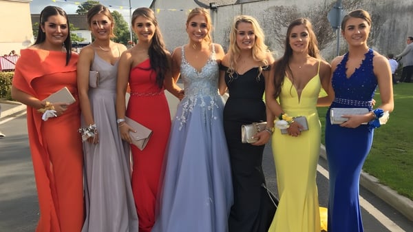 Un grupo de jóvenes mujeres en vestidos formales posan afuera frente a un edificio en el terreno de la Presentation Secondary School Kilkenny.