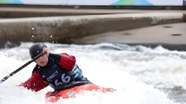 Un estudiante de la Presentation Secondary School navega con un kayak rojo y azul por un río de aguas bravas junto a una estructura de hormigón.