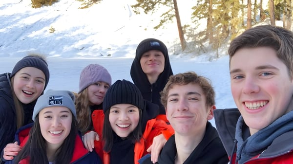 Estudiantes de la Prince of Wales Secondary School están juntos en el bosque nevado con ropa de invierno cálida.