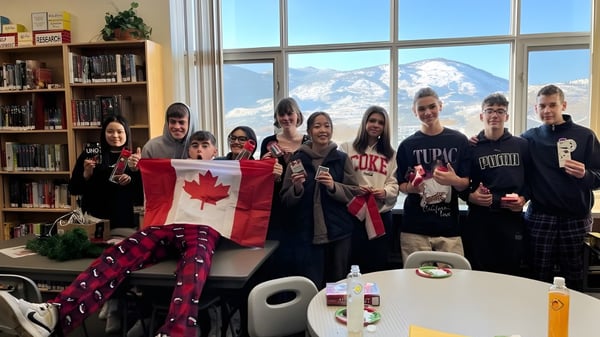Un grupo de estudiantes de la Princess Margaret Secondary School sostiene una bandera canadiense en una sala de descanso con vista a montañas nevadas.