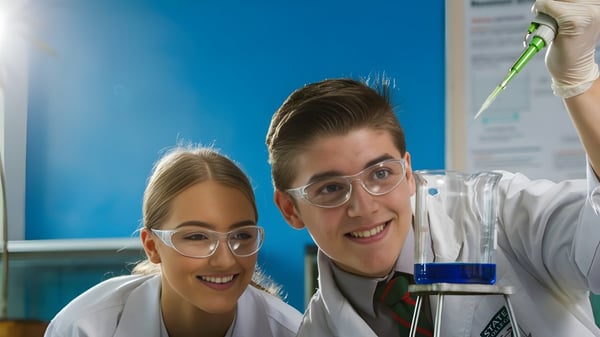 Dos estudiantes del Prior Park College llevan batas de laboratorio y gafas de protección en el laboratorio y miran a la cámara.