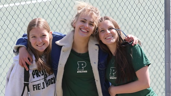 Tres estudiantes de la Proctor Academy se abrazan riendo frente a una cerca de alambre.