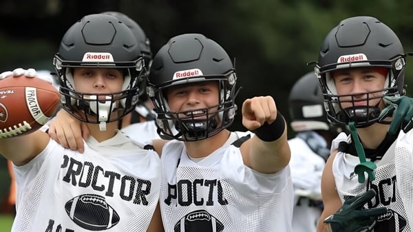 Tres estudiantes de la Proctor Academy en uniformes de fútbol están juntos sosteniendo un balón de fútbol en un campo deportivo.