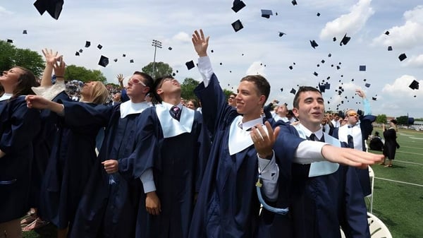 Los graduados de la Prospect High School lanzan sus birretes azules al aire en el campo deportivo.
