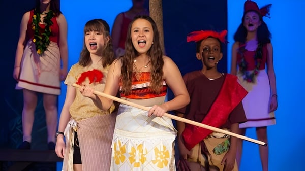 Un grupo de alumnas de la Providence Christian Academy se presenta en el escenario frente a un fondo azul con trajes coloridos.