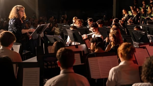 Una gran orquesta toca en el escenario de la Providence Christian Academy frente a un público visible.