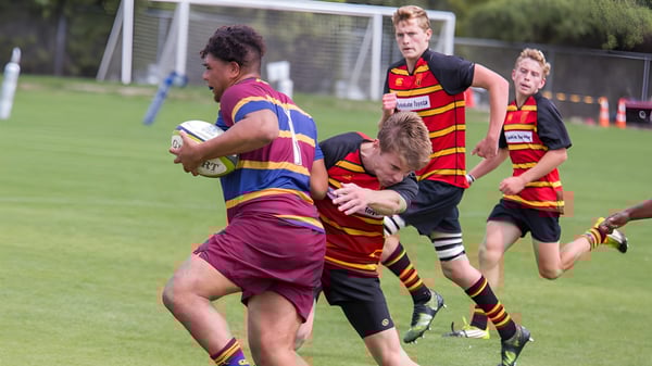 Estudiantes de la Pukehohe High School juegan rugby en un campo deportivo y realizan un tackle durante el juego.