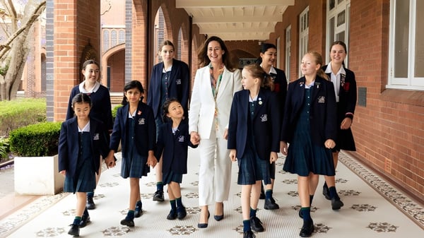 Un grupo de alumnas está en el pasillo del Pymble Ladies College frente a paredes de ladrillo y ventanas arqueadas.