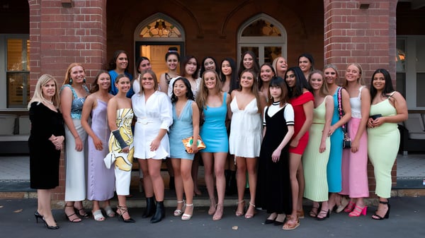 Un grupo de jóvenes mujeres con vestidos coloridos está frente a un edificio de ladrillo en el campus del Pymble Ladies College.