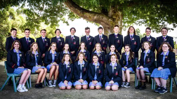 Un grupo de estudiantes de la Queechy High School está junto a un gran árbol en un terreno parecido a un parque.