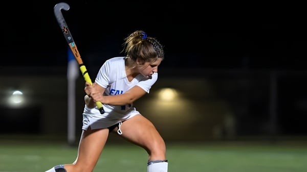 Una deportista de la Queen Anne’s School sostiene un stick de hockey en un campo iluminado por la noche.