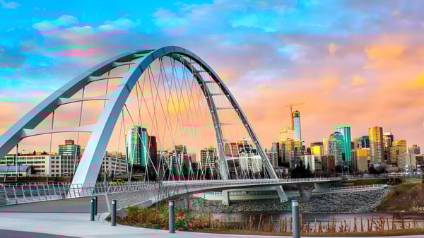 Un moderno puente de arco cruza un río con un panorama de la ciudad detrás del campus de la Queen Elizabeth High School al atardecer.